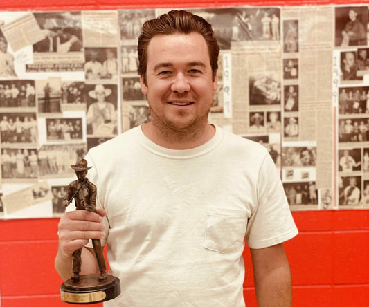 Photo of Luke Price smiling and holding the first place trophy at the National Fiddle Old Time Championships.
