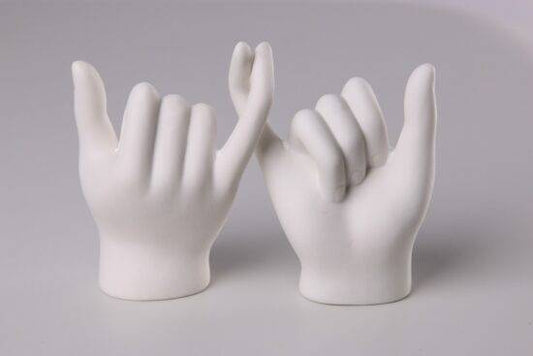 A white sculpture of two hands with intertwined pinky fingers.